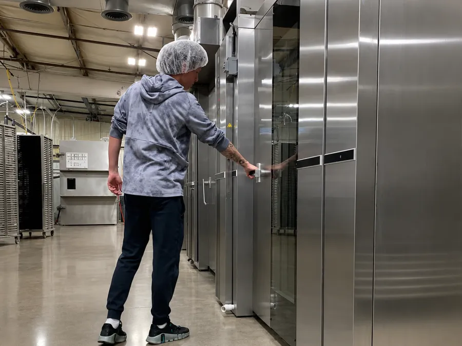 A Flatiron Food Factory worker in a hairnet opening a stainless steel freeze-dryer door